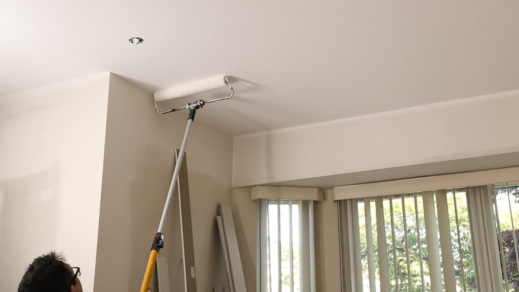 Painter rolling flat white paint on a living room ceiling in a San Diego home